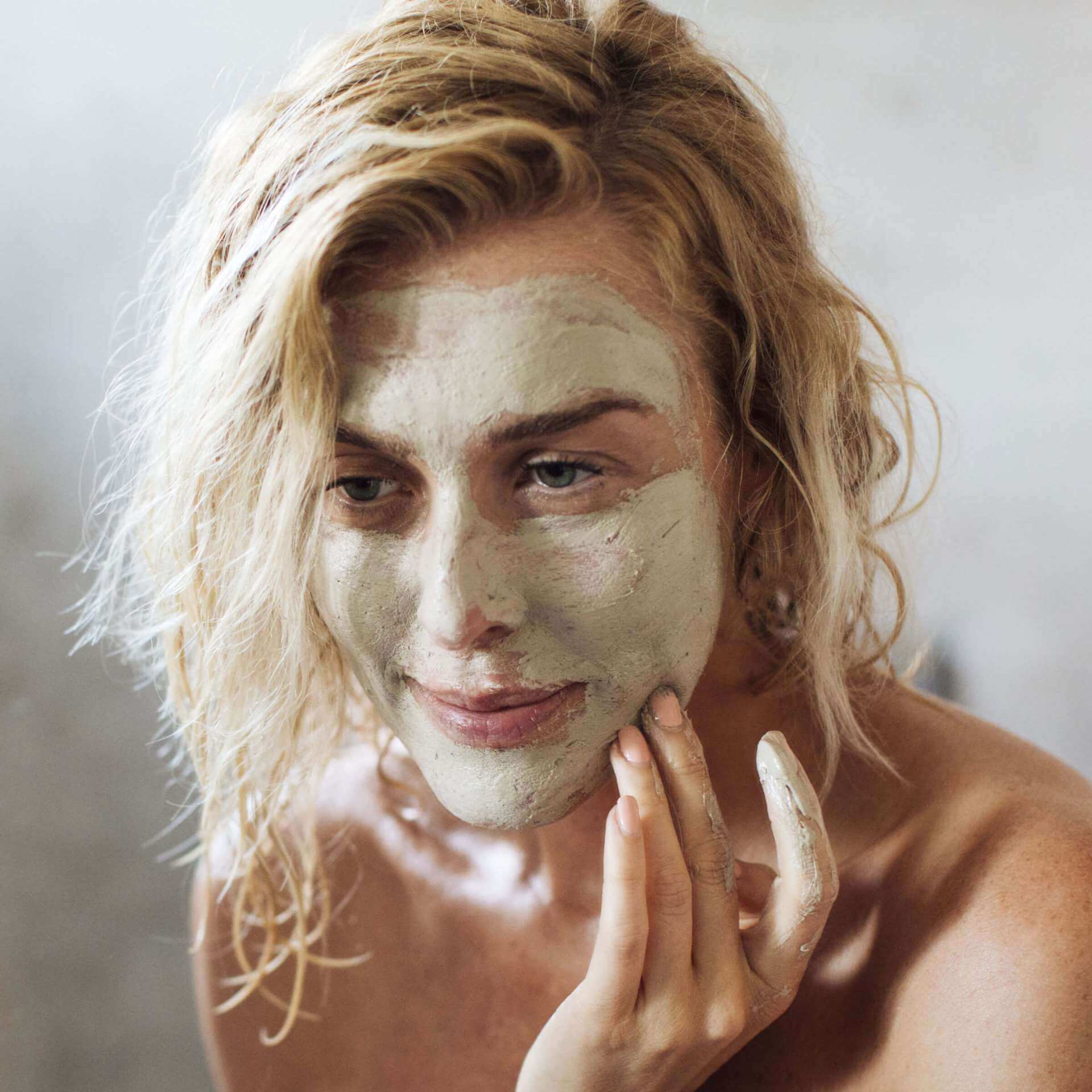 Girl with blonde hair applying green clay mask