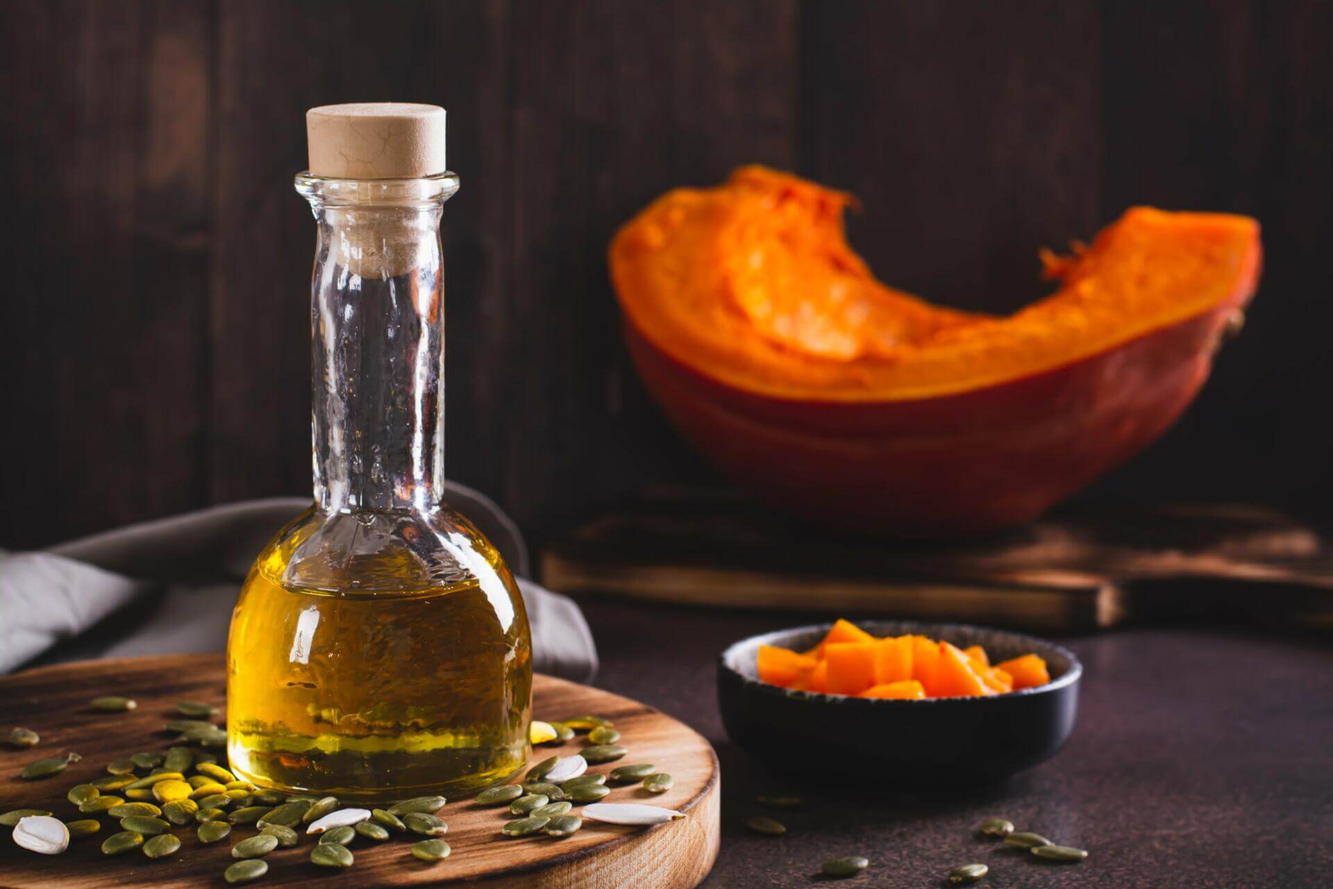 Glass bottle of pumpkin seed oil with pumpkin pieces and scattered pumpkin seeds on a wooden board