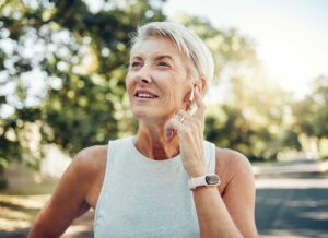 Older woman adjusting wireless earbud outdoors