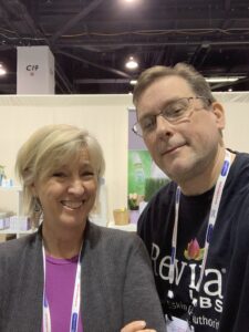 Two people smiling at a convention booth.