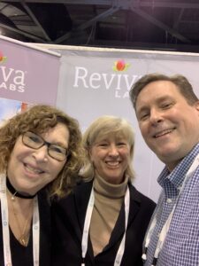 Smiling people at a Reviva Labs conference booth.