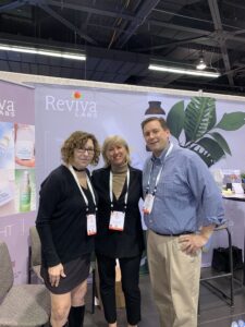 Three people at Reviva Labs booth smiling.