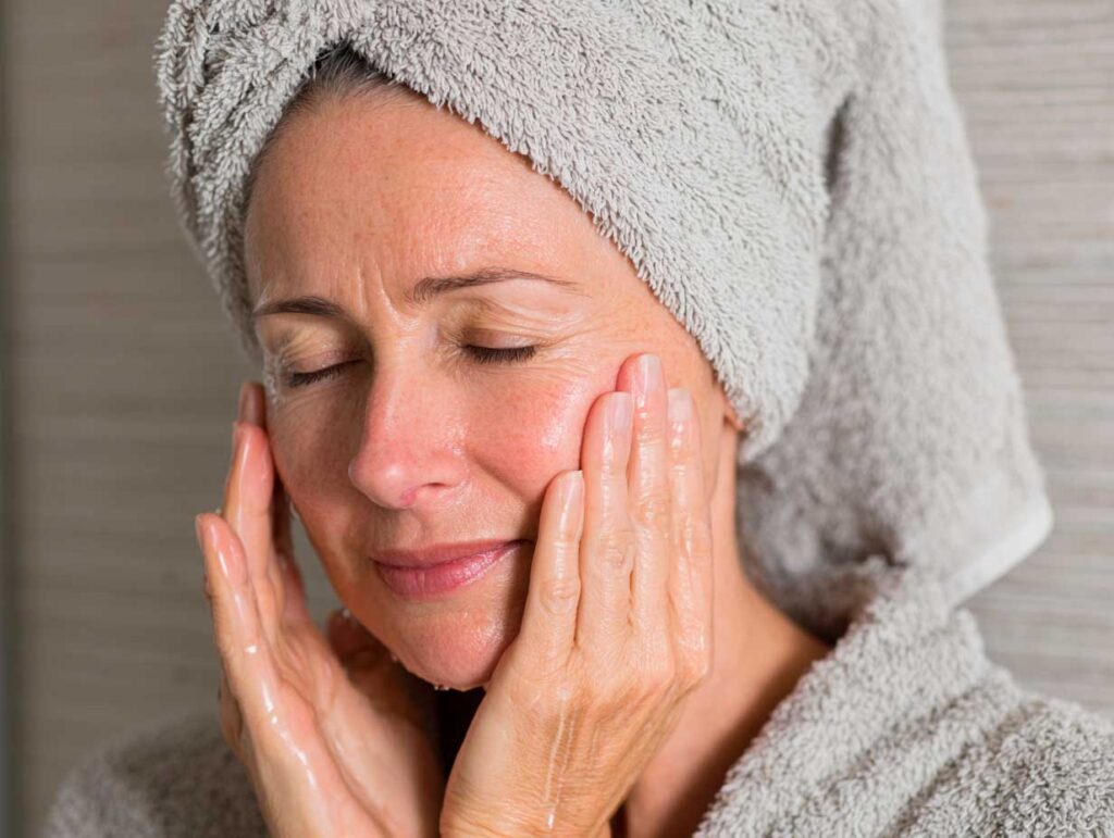 Woman cleansing face with towel wrapped head.
