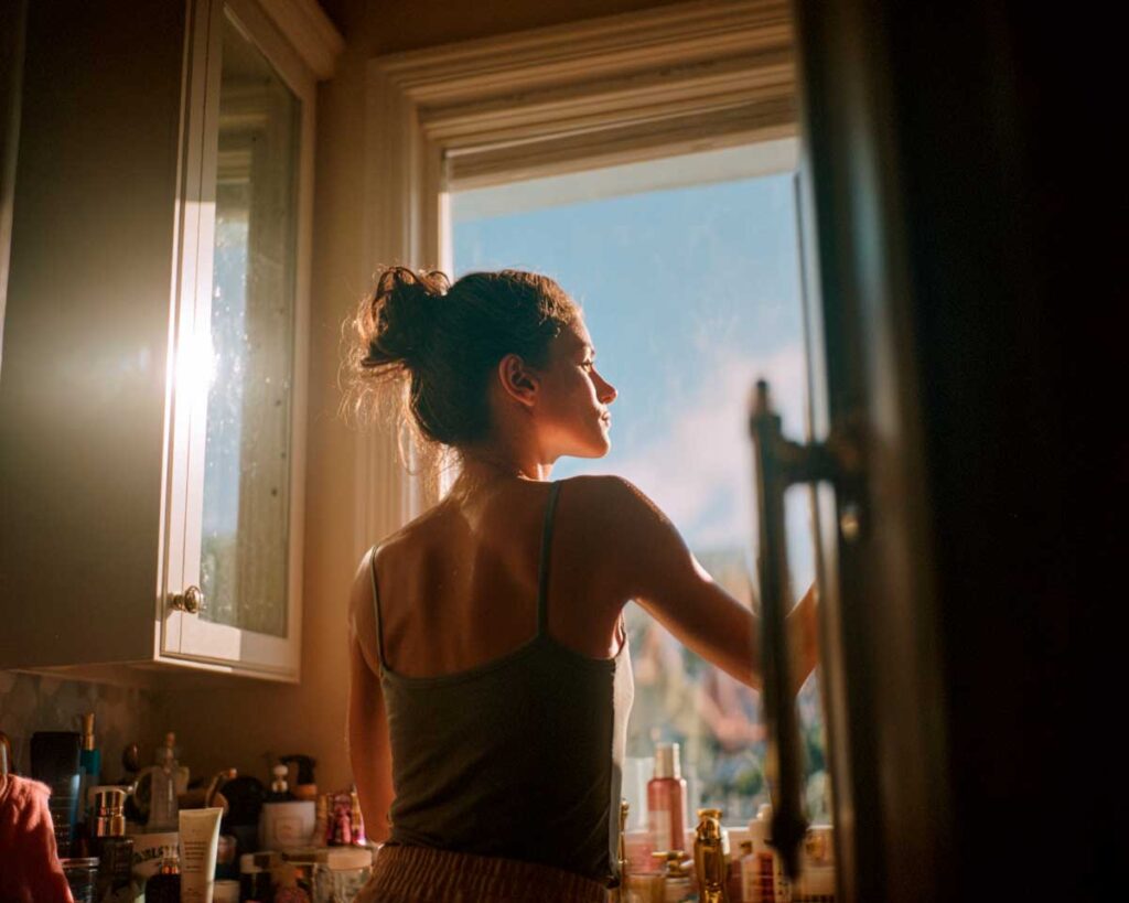 Woman standing by sunlit window in bathroom