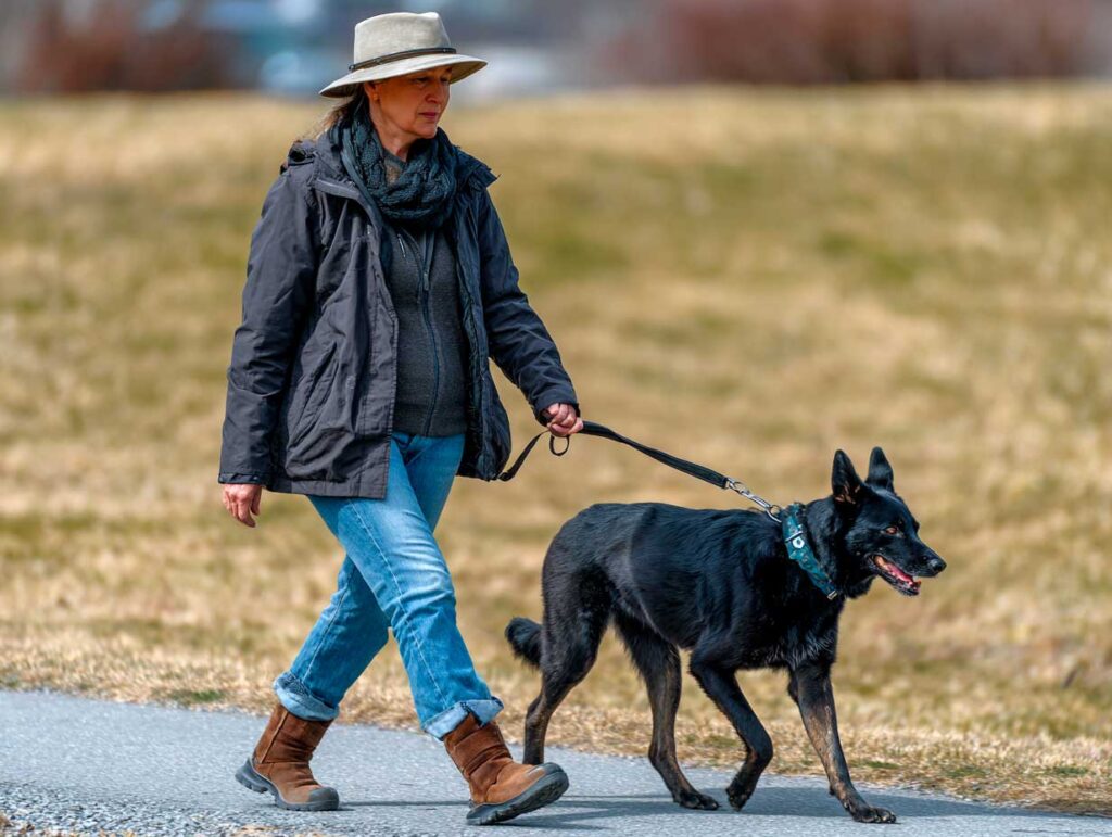 Woman walking a black dog on a path