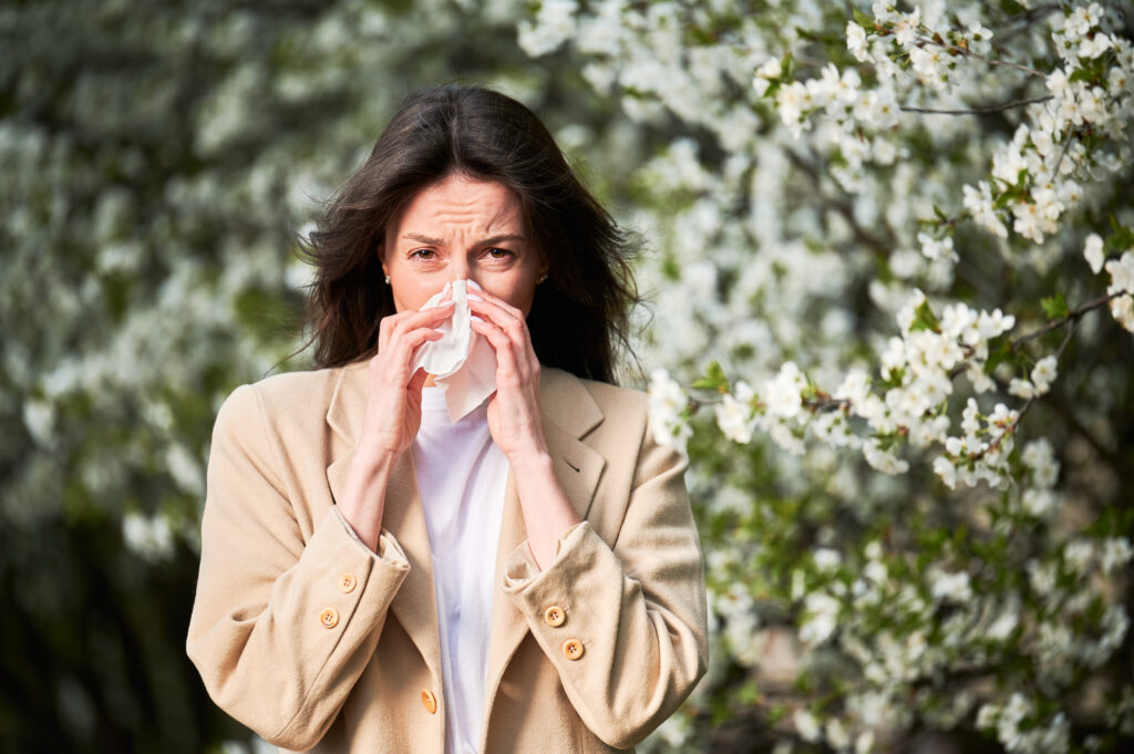 Woman sneezing near blooming spring flowers