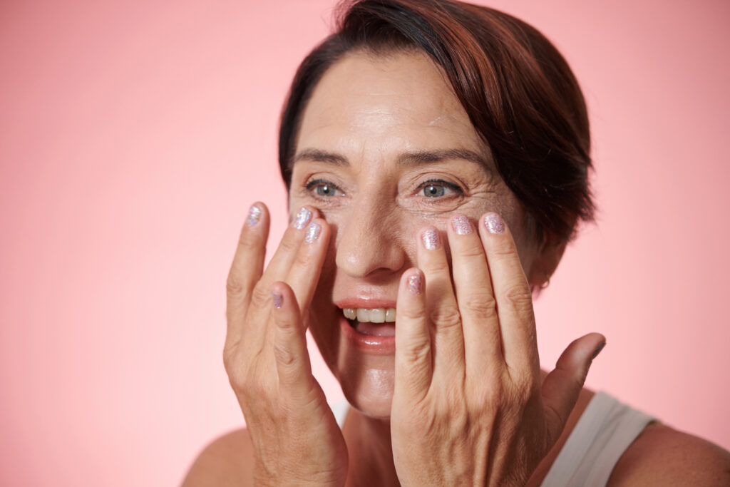 Woman applying skincare cream to face on pink background