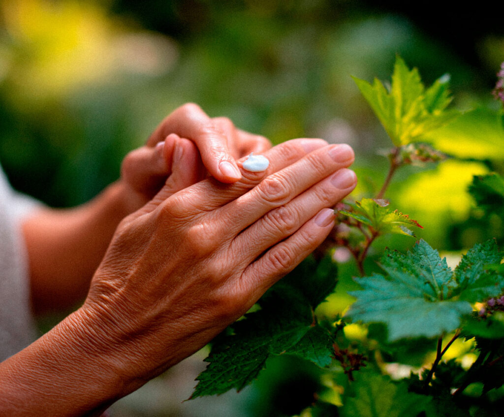 Hands applying lotion beside green garden plants