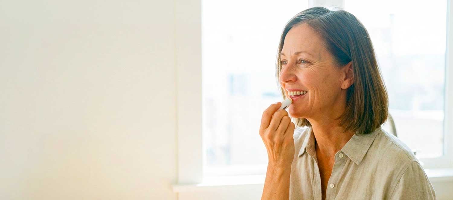 Woman applying lip balm near a bright window
