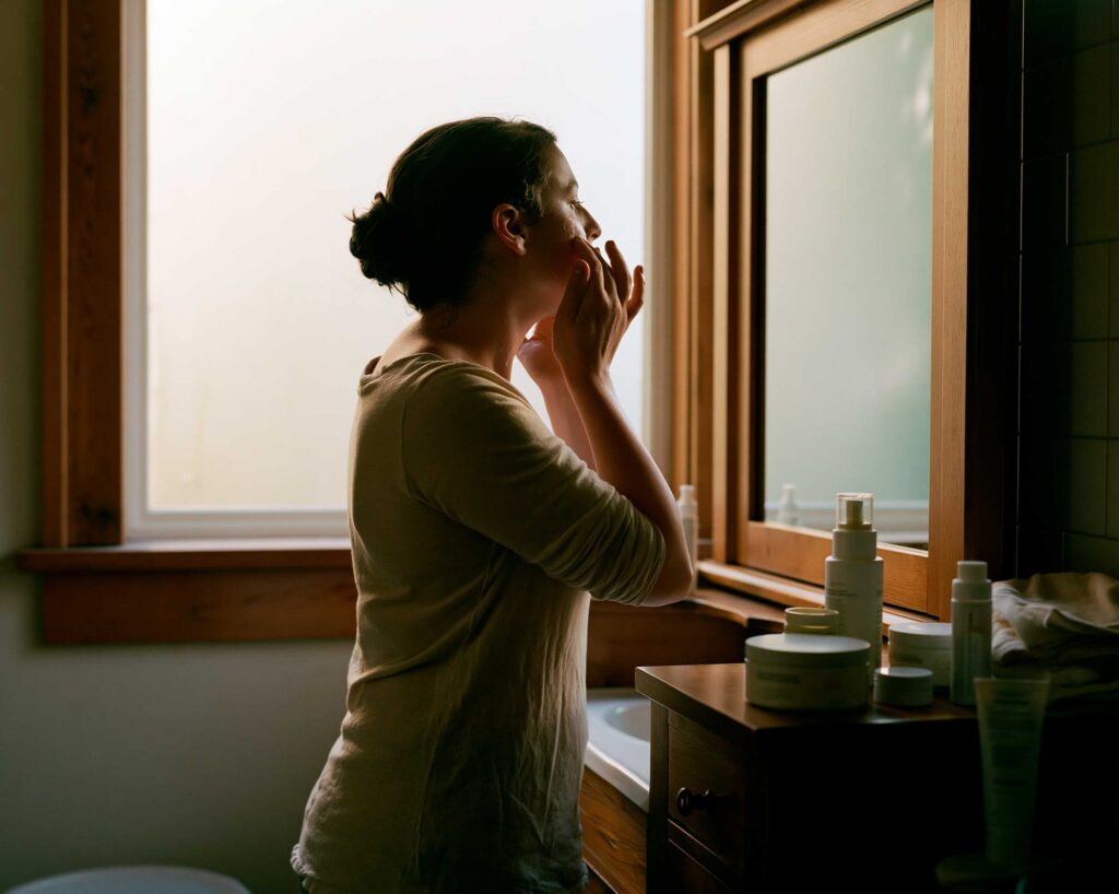 Woman applying skincare in bathroom mirror