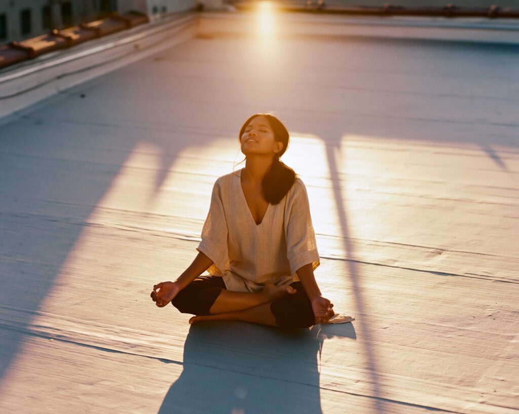 Woman meditating cross-legged at sunset on rooftop