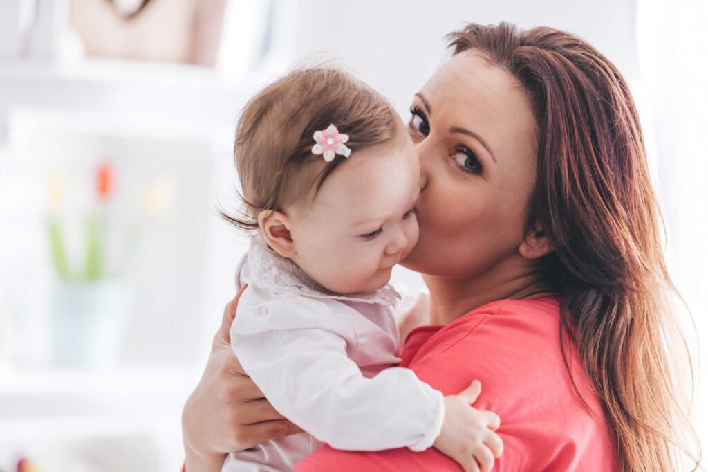 Mother kissing baby while holding her indoors