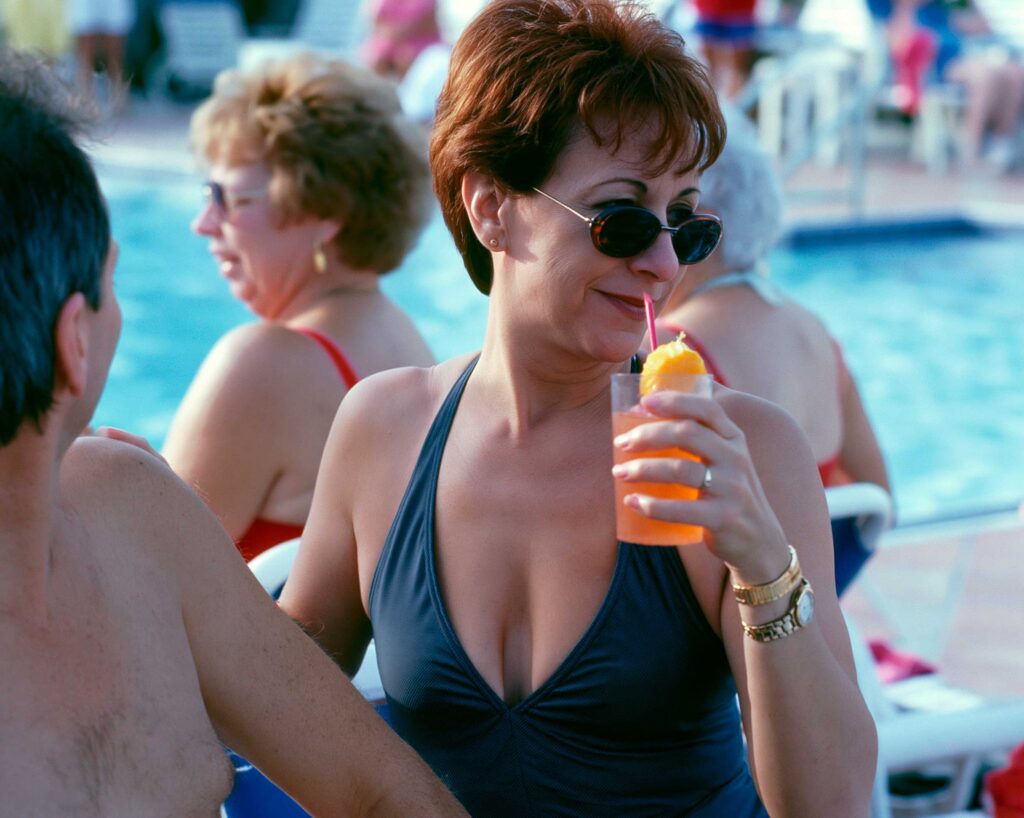Woman in sunglasses holding orange drink by pool
