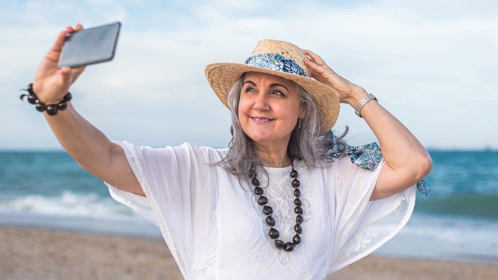 Woman taking selfie on beach wearing straw hat