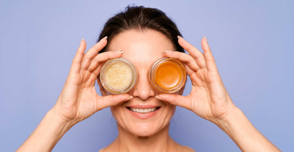Woman holding skincare jars over eyes smiling
