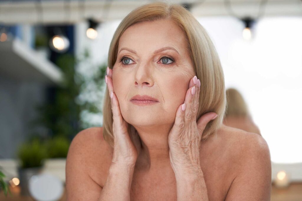 Mature woman examining her facial skin in mirror