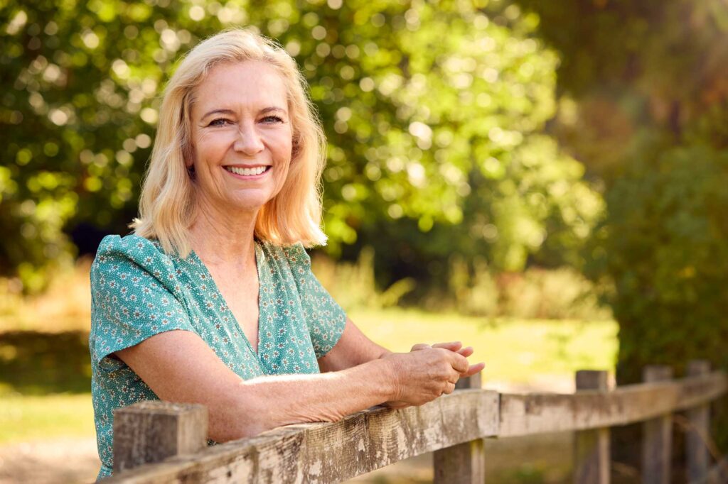 Smiling woman leaning on fence in sunny park