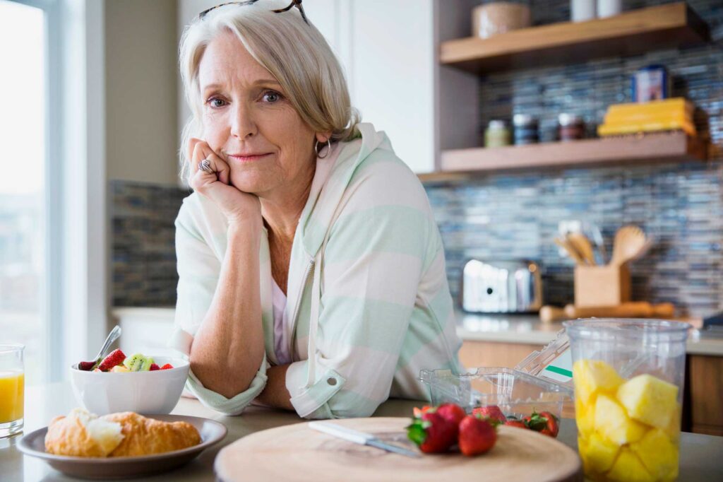 Older woman leaning on kitchen counter with fruit