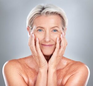 Smiling older woman touching face against gray background