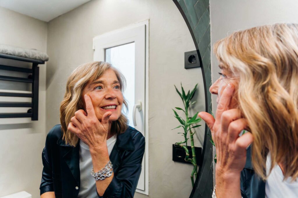Older woman smiling at reflection, touching her cheek
