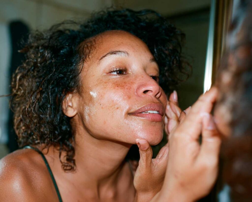 Woman applying facial serum while looking in mirror