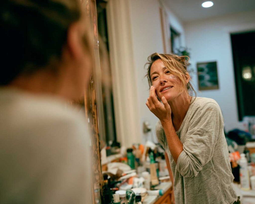 Woman applying face cream in bathroom mirror