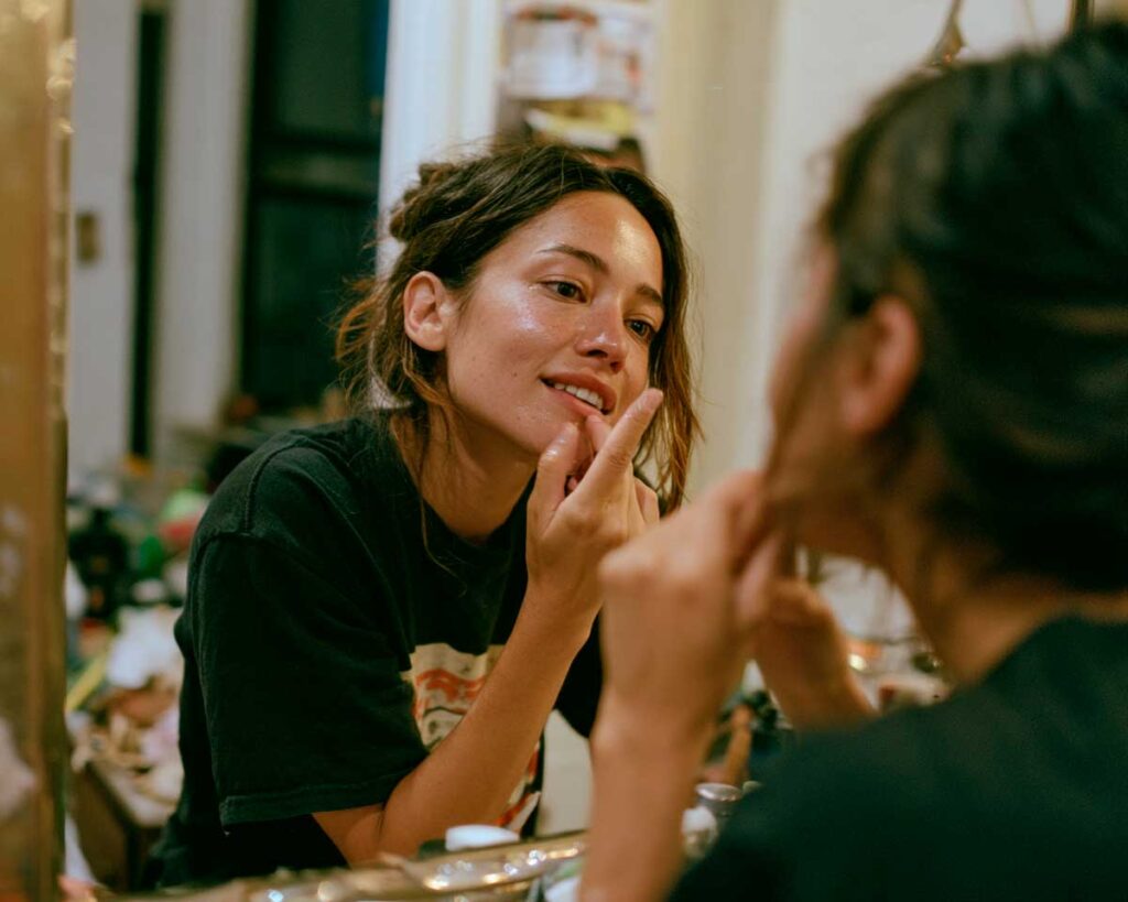 Woman applying skincare while looking in bathroom mirror