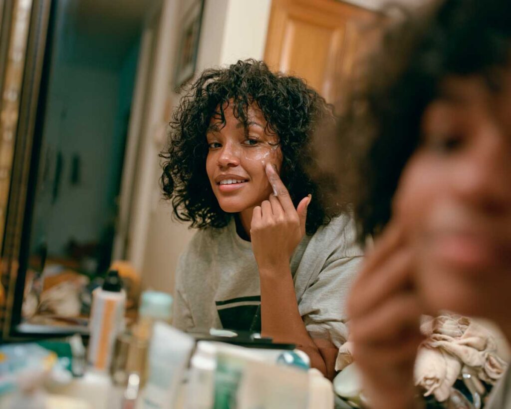 Woman applying facial cream in bathroom mirror