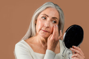 Older woman examining skin in handheld mirror