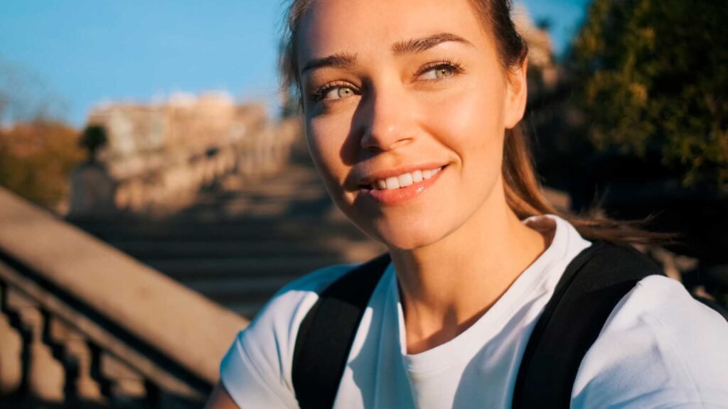 Smiling woman outdoors at sunset with backpack