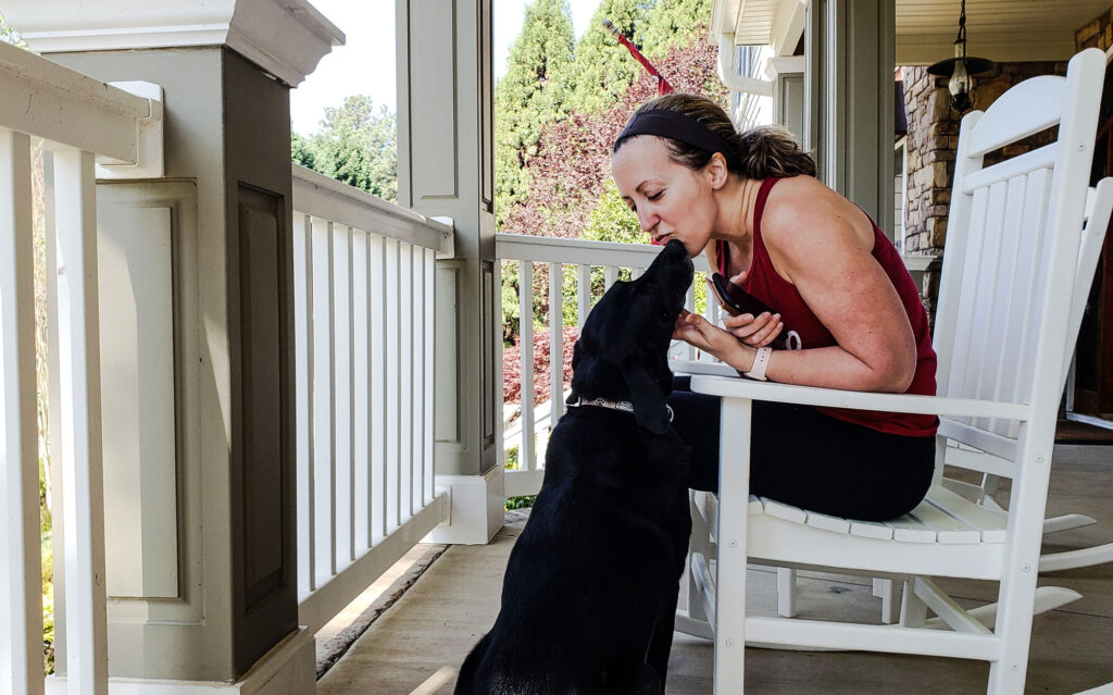 woman cuddles black dog on suburban porch 2026 01 09 00 03 17 utc
