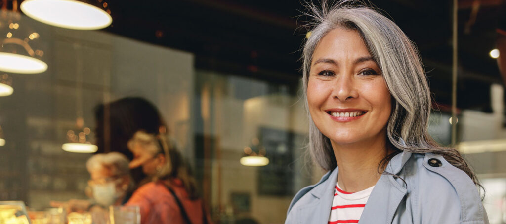 Smiling gray-haired woman outside a warmly lit café