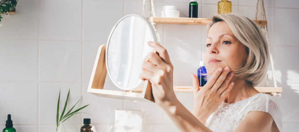 Woman applying facial skincare while looking in bathroom mirror