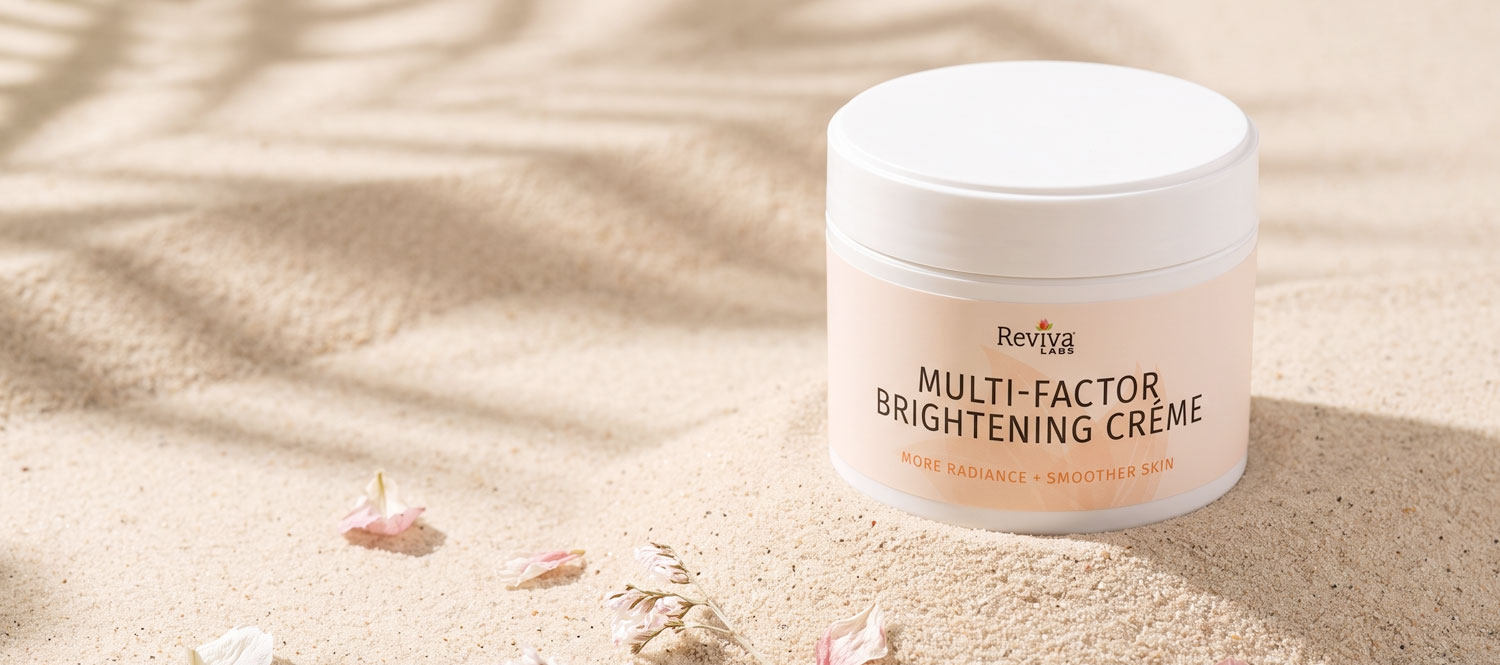 Reviva Labs brightening cream jar displayed on sunlit sand