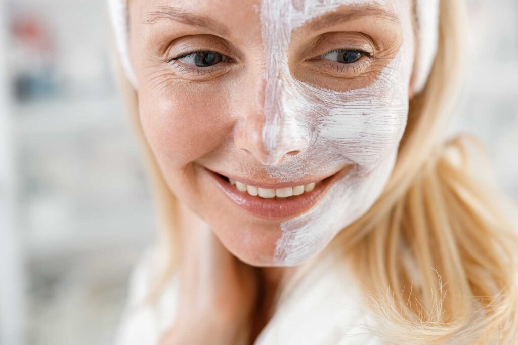 Smiling woman applying white facial mask