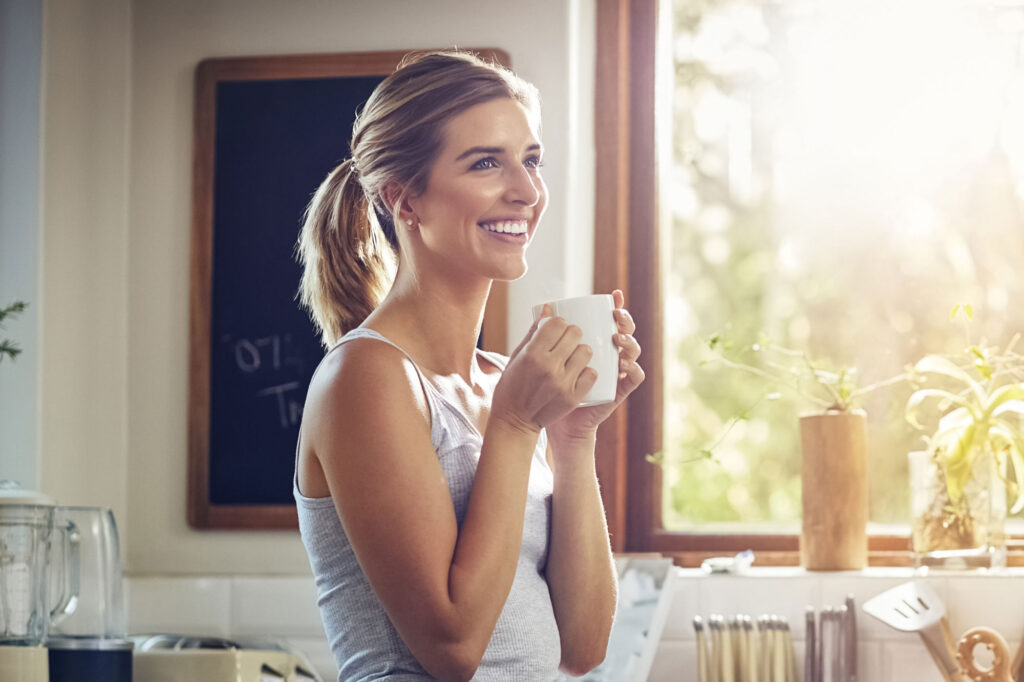 Smiling woman holds mug in sunlit kitchen
