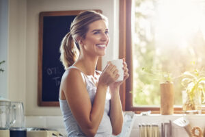 Smiling woman holds mug in sunlit kitchen
