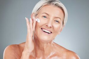 Smiling older woman applying moisturizer beneath her eye