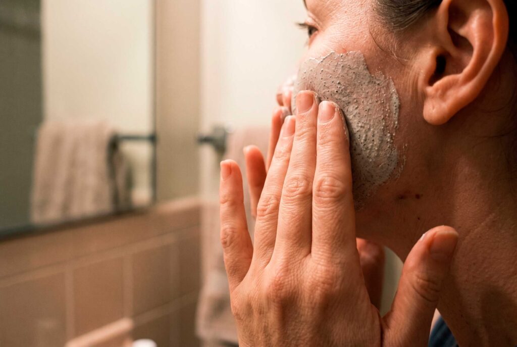Woman applying exfoliating facial scrub to cheek
