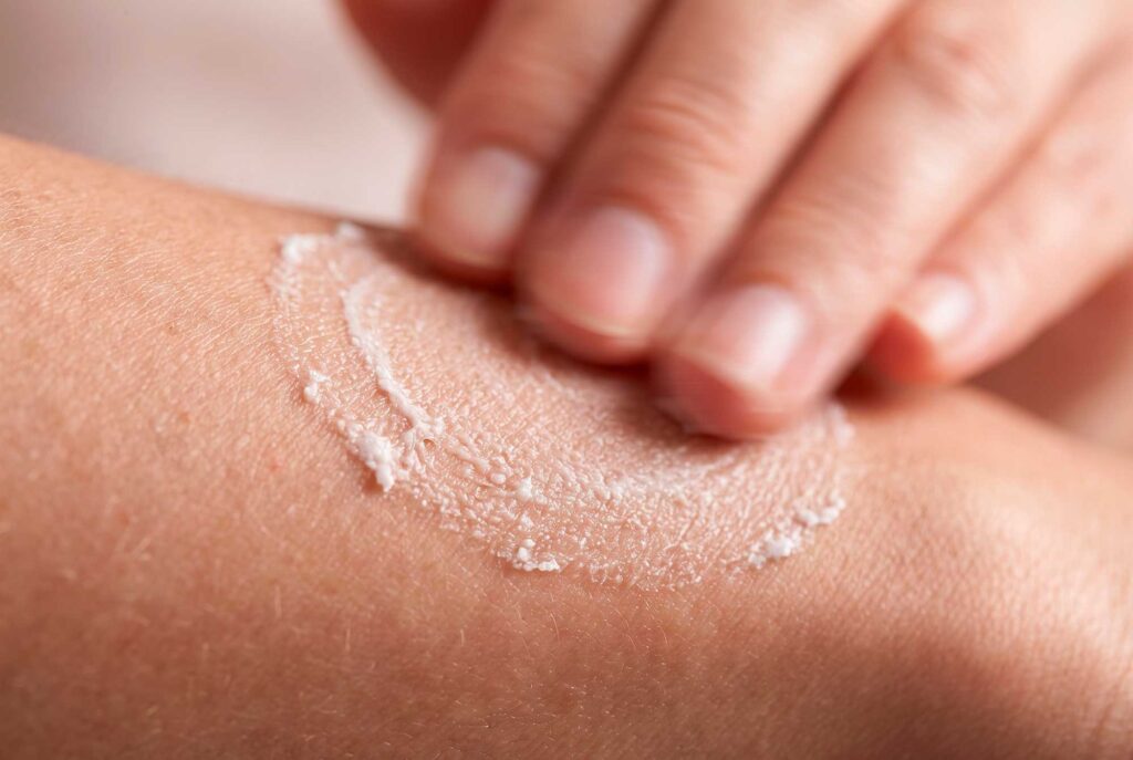 Hand applying white exfoliating cream to skin