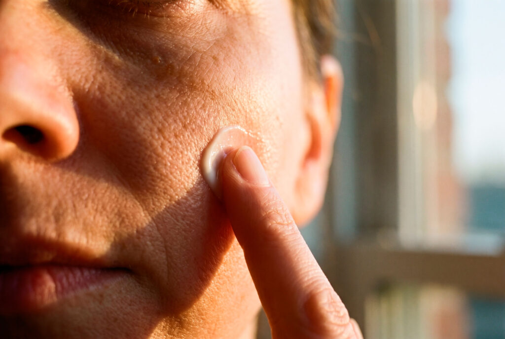 Person applying cream to cheek in sunlight
