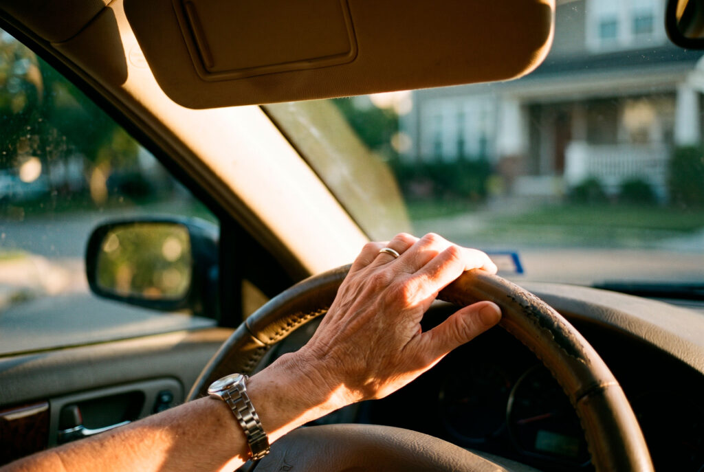 Hands gripping steering wheel in sunlit car interior