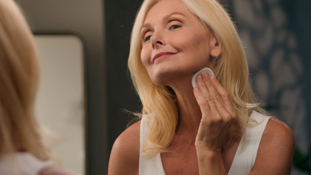 Woman applying skincare to neck with cotton pad