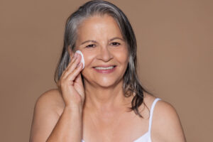 Smiling mature woman applying cotton pad to cheek