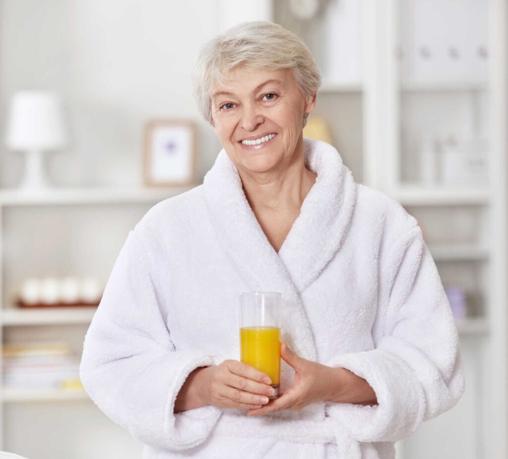 Smiling older woman in bathrobe holding orange juice
