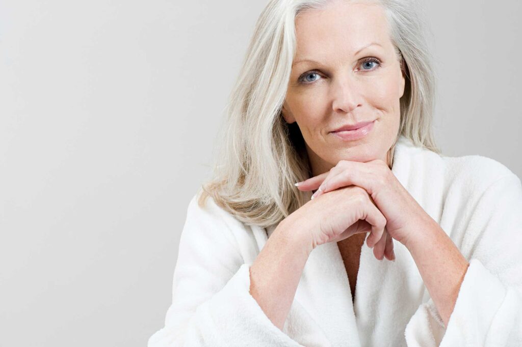 Smiling older woman in white robe with clasped hands