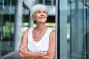 Smiling older woman standing beside a glass building entrance