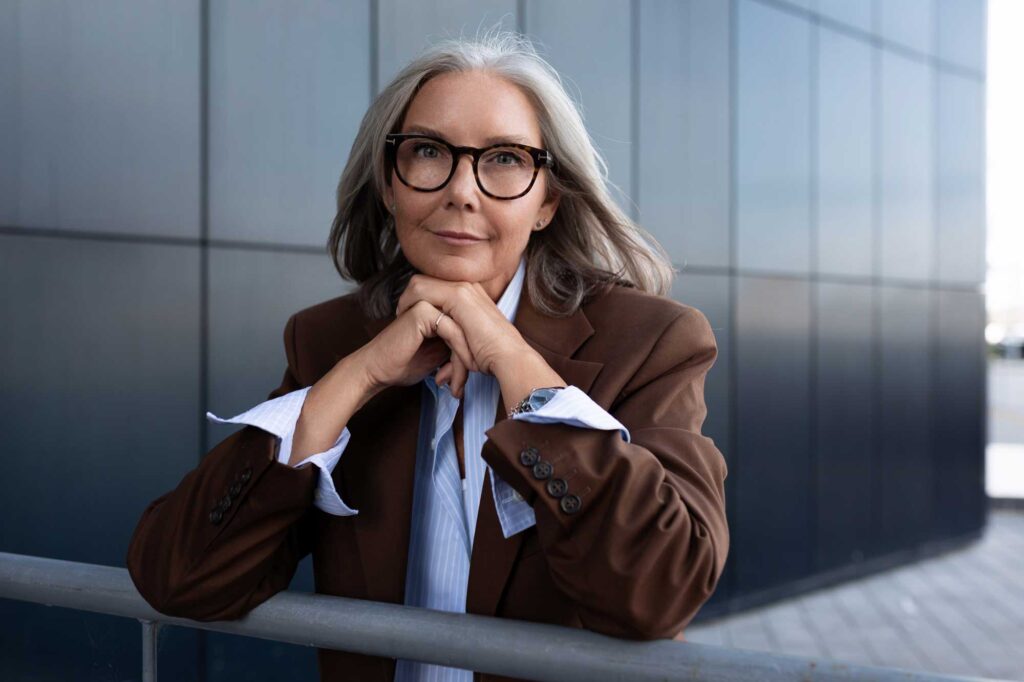 Confident gray-haired businesswoman in glasses leaning on railing