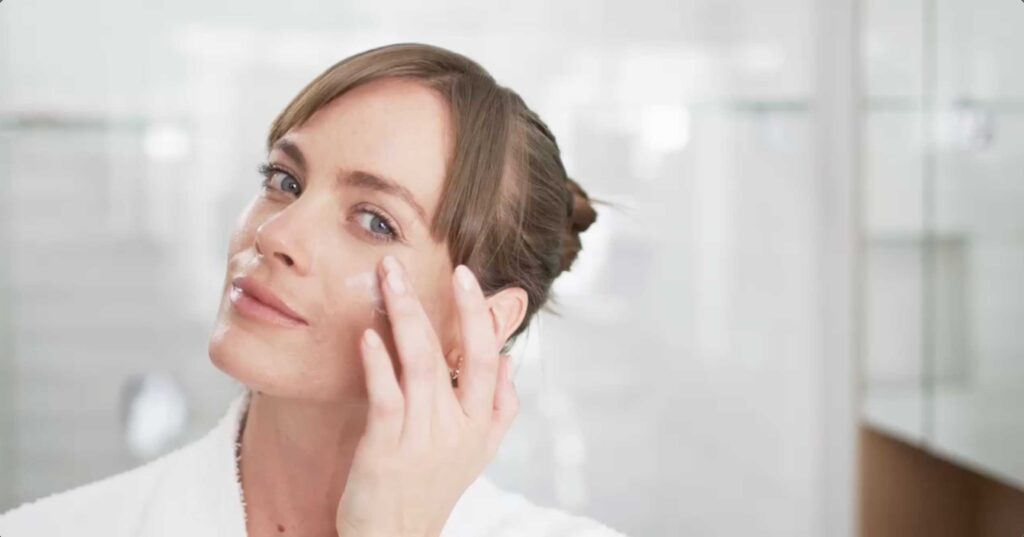 Woman applying facial cream in bright bathroom