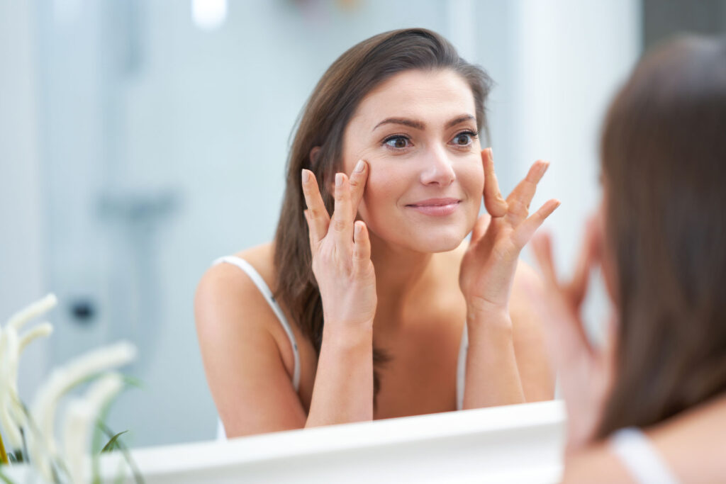 Woman gently applying eye cream while looking in mirror
